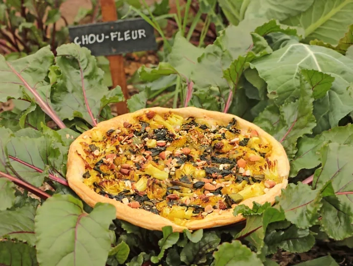 Une tarte aux légumes posée dans le potager à côté d'un panneau indiquant « chou-fleur »